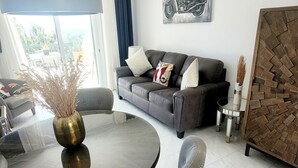 Un salon moderne avec une table à manger ronde, un canapé recouvert d’un tissu gris et une grande fenêtre agrémentée de rideaux.