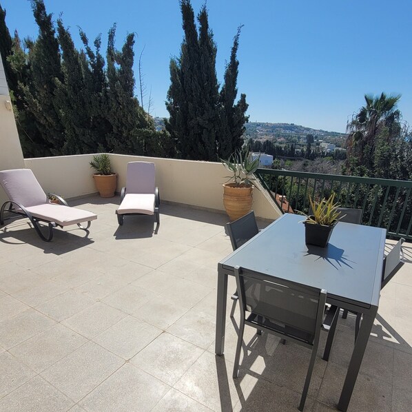 A balcony with two lounge chairs, a table, and potted plants. - PJ's Apartment ,Chlorakas, Paphos. 2 Bedrooms with a large south facing veranda. (Chloraka)