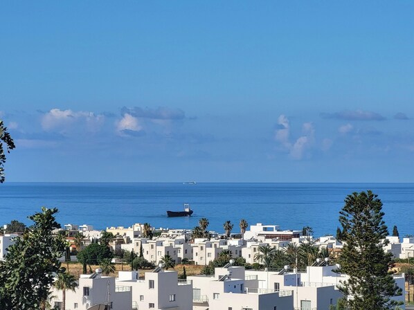 Un quartier résidentiel en bord de mer, avec des bâtiments modernes aux façades blanches, un ciel bleu dégagé et un bateau sur la mer.