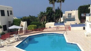Une piscine rectangulaire dont les bords sont recouverts de carreaux, entourée d’une clôture rouge et située à côté d’un bâtiment doté de balcons.