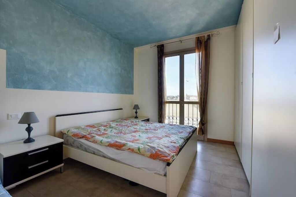 A bedroom with a bed, nightstand, lamp, and a window with curtains.