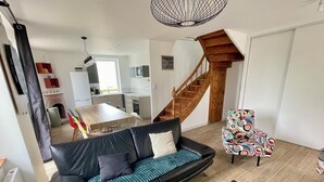 A modern living room with a black leather sofa, a colorful patterned armchair, and a staircase leading to a loft area. - Superbe Maison Moderne Entièrement Rénovée Trégomeur Proche Mer - Chez Alphonse (Trégomeur)
