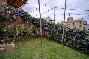 A garden with a wooden fence, a brick building, and a grassy area. - Franca's House - Piscina - Praia do Rosa (Imbituba)