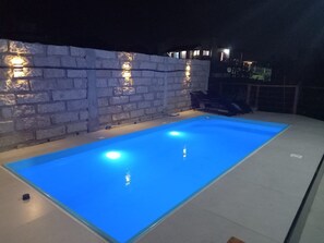 A rectangular swimming pool with blue lighting, surrounded by a stone wall with embedded lights. - Franca's House - Piscina - Praia do Rosa (Imbituba)