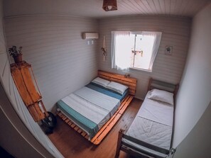 A compact room with a single bed, a small window, and a wall-mounted air conditioner. - Franca's House - Piscina - Praia do Rosa (Imbituba)