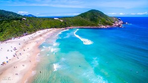 A beach with clear turquoise waters, a sandy shore, and a mountainous backdrop. - Franca's House - Piscina - Praia do Rosa (Imbituba)