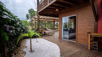 A wooden deck with a hammock, a small palm tree, and a patio area with a table and chairs.