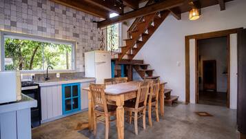 A kitchen with a dining table and chairs, a refrigerator, and a wooden staircase.