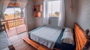 A room with a bed, a bench, a window with curtains, and a view of the outside. - Franca's House - Piscina - Praia do Rosa (Imbituba)