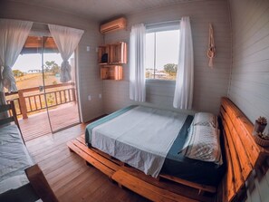 Ein Zimmer mit einem Bett, einer Sitzbank, einem Fenster mit Vorhängen und Blick ins Freie.