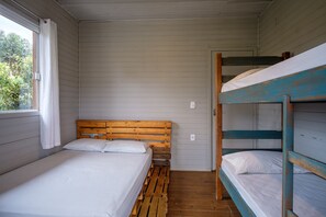 A single bed with a wooden headboard, a bunk bed with blue railings, and a window with curtains.