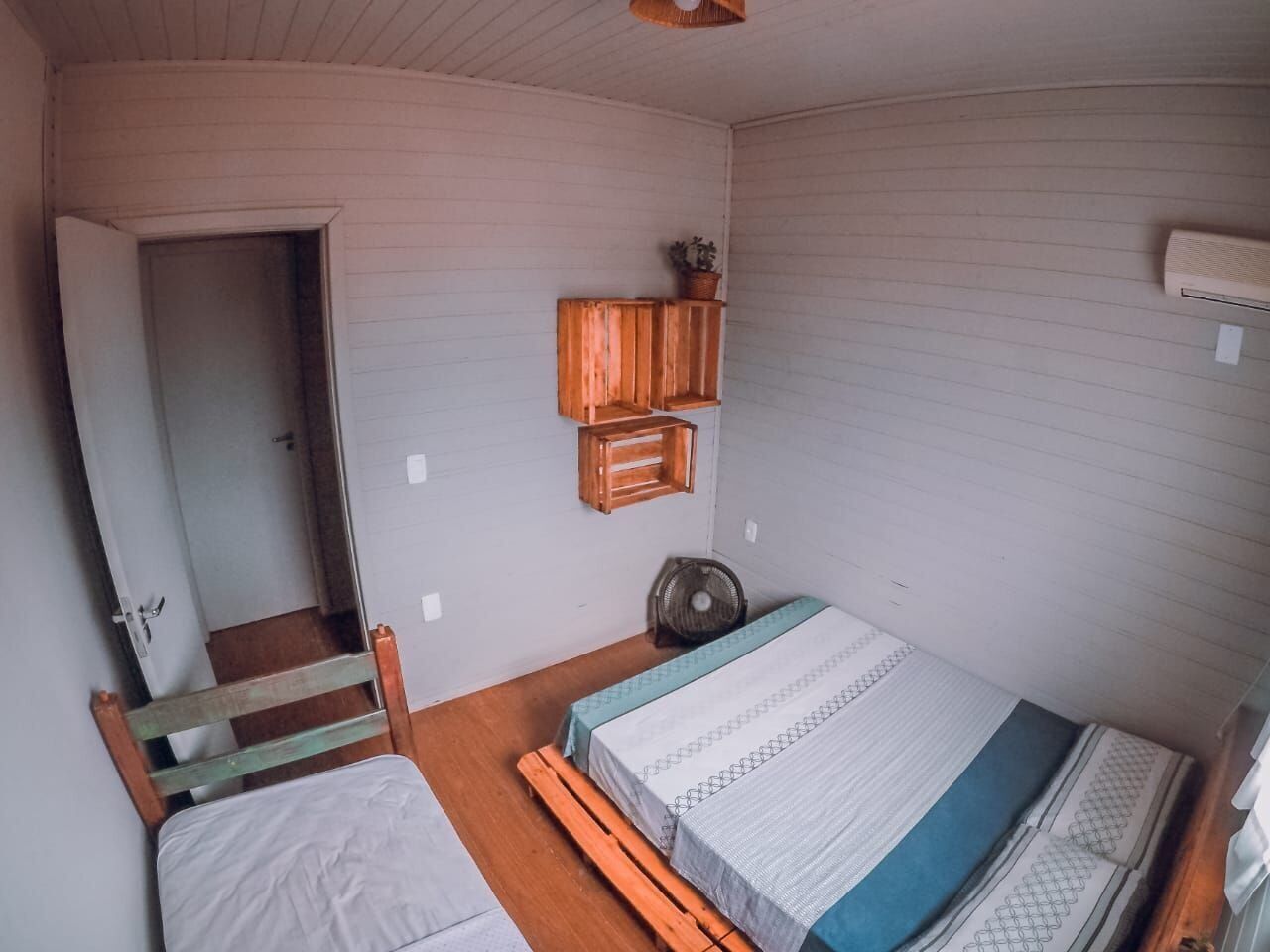 Een kamer met een bed, een houten bankje, een ventilator en een plank met een plant.