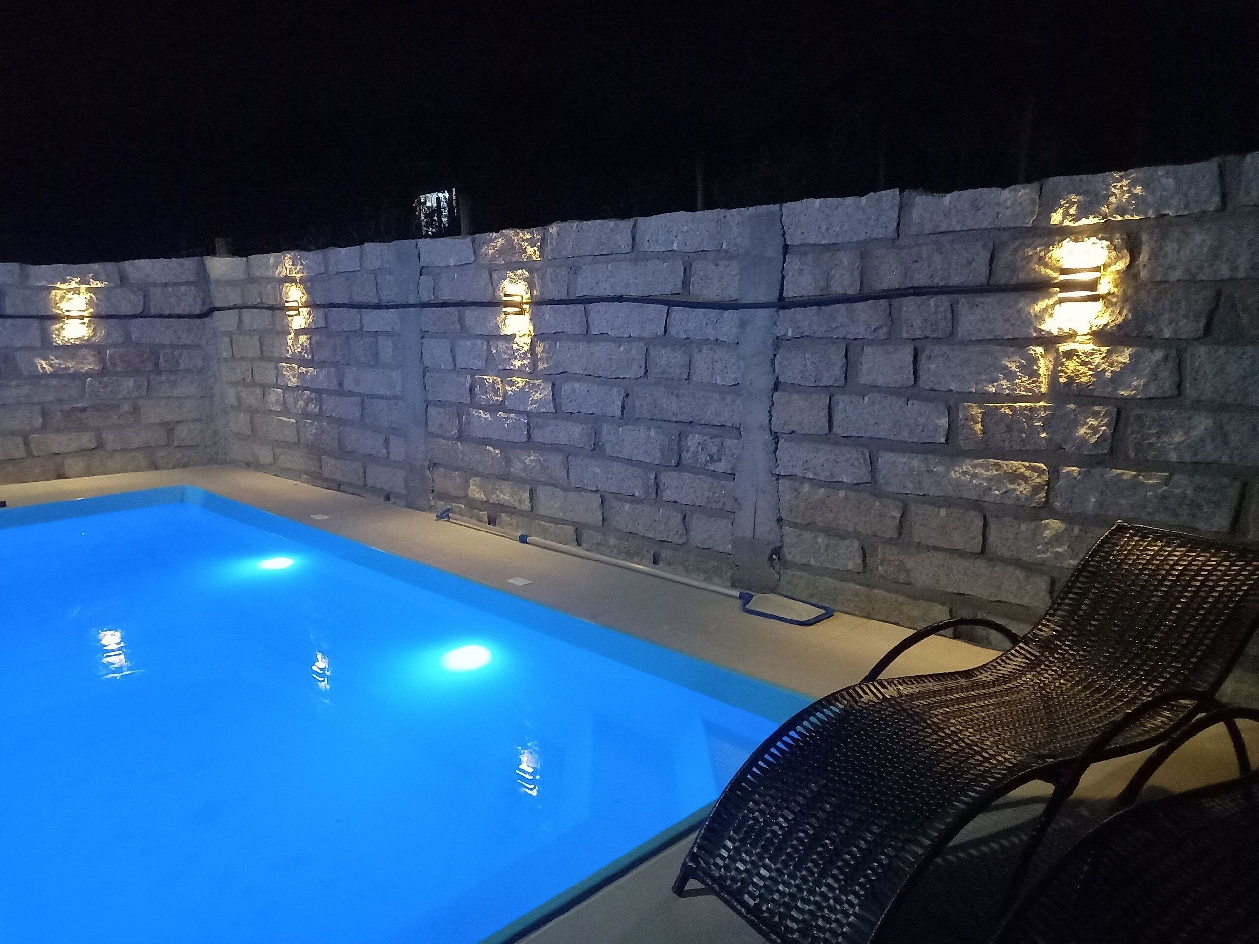 Una piscina exterior con muro de ladrillo e iluminación integrada.