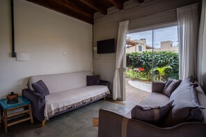 A room with a sofa, a small table, a TV mounted on the wall, and a view of the outside.