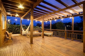 Eine Holzterrasse mit Bänken und einer Hängematte, unter einer Holzpergola mit Lichterketten.