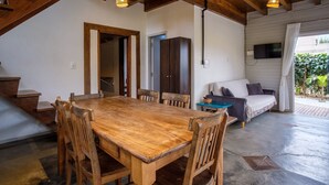 A spacious room with a wooden dining table and chairs, a sofa, and a television mounted on the wall. - Franca's House - Piscina - Praia do Rosa (Imbituba)
