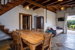 Ein geräumiges Zimmer mit einem Holzessttisch und -stühlen, einem Sofa und einem an der Wand montierten Fernseher.