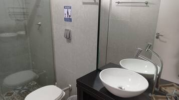 A bathroom with a toilet, a sink, a glass shower enclosure, and a mirror.