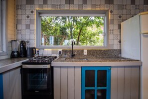 A kitchen with a window, a stove, a sink, and cabinets.