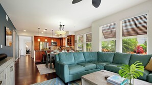 A modern living room with a sectional sofa, a coffee table, and a dining area with a kitchen in the background.