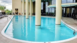 A pool area with clear blue water, surrounded by lounge chairs and tables, and a building with large windows in the background.