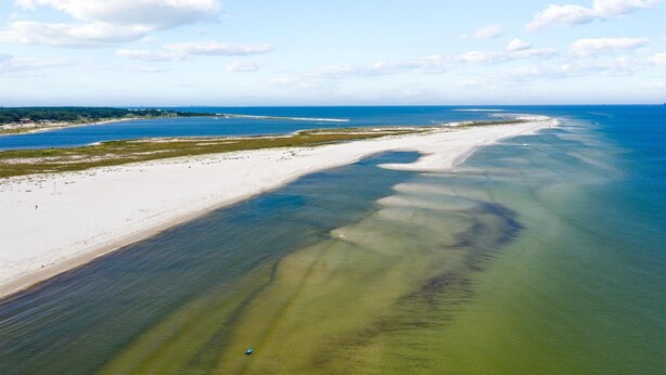 An aerial view of a coastal area with a sandy beach and clear blue waters.