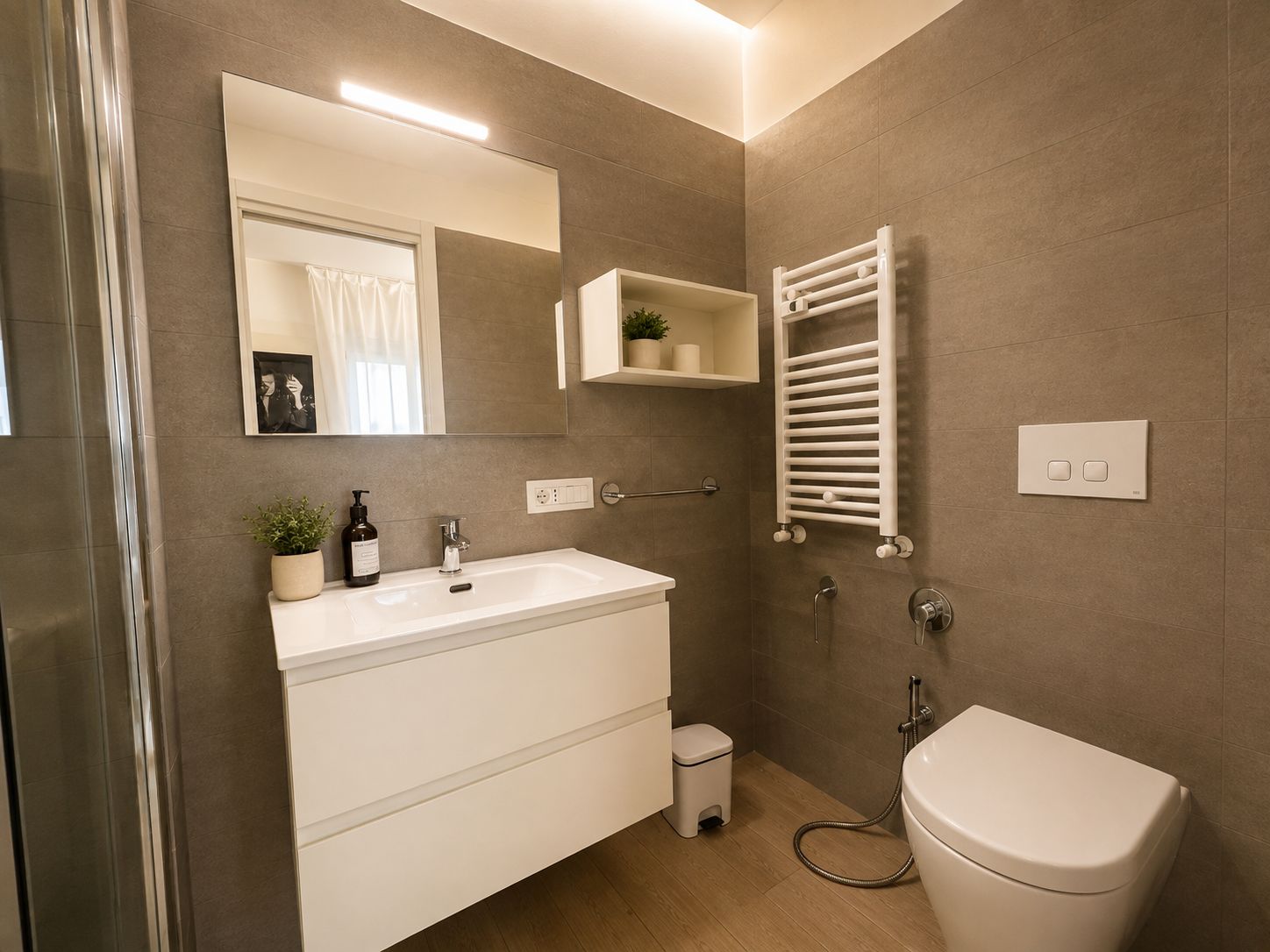 A modern bathroom with a white vanity, a mirror, a towel rack, and a toilet.