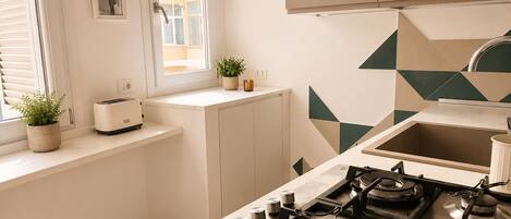 A modern kitchen with a gas stove, a toaster, and a window with blinds.