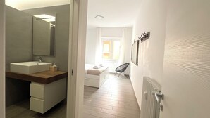 A modern bathroom with a large mirror, a sink, and a toilet. There is a chair in the adjacent room and a radiator on the wall. - Agliardi House at the Vatican (ROMA)