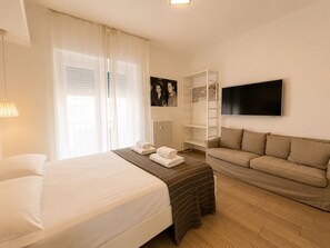 A hotel room with a bed, a sofa, a television, and a window with curtains.