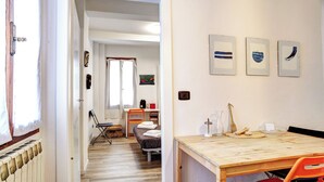 Una habitación con suelo de madera, una mesa de comedor con sillas, un radiador y una ventana con cortinas.
