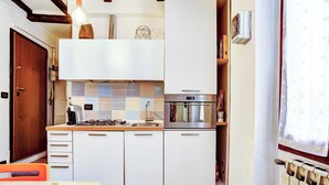 Una cocina compacta con armarios blancos, estufa a gas, horno empotrado y salpicadero de azulejos.