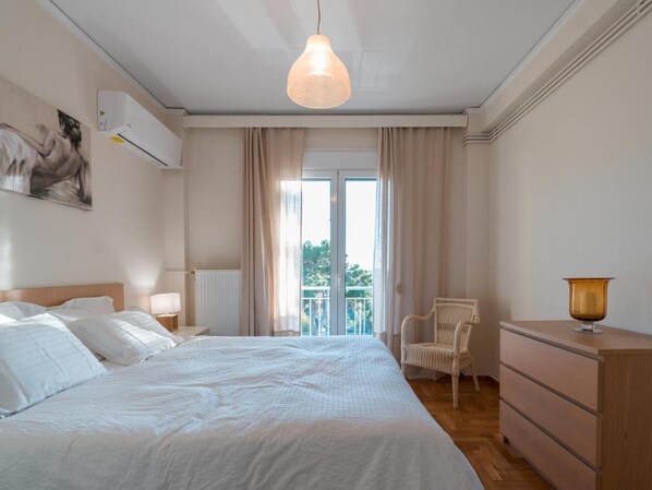 A bedroom with a large bed, a chair, a dresser, and a window with curtains.