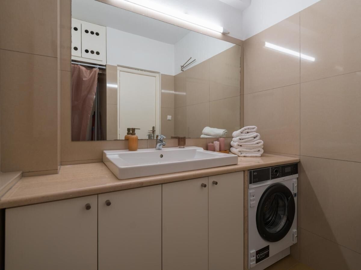 A bathroom with a sink, mirror, and washing machine.