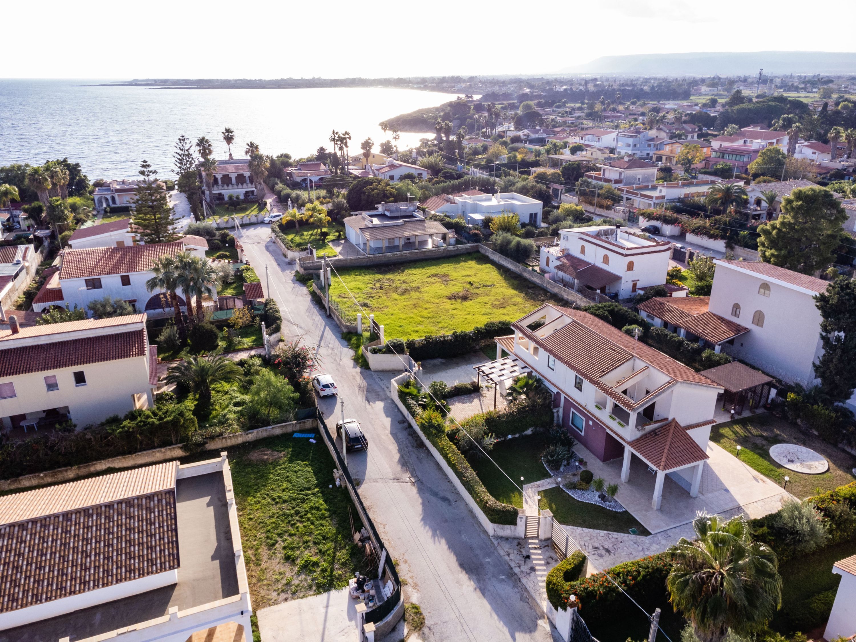 An aerial view of a residential area with houses, a road, and a body of water in the background.