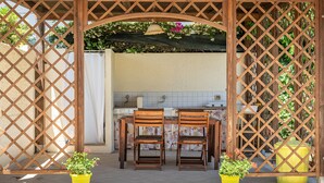 A covered outdoor area with a wooden lattice structure, two wooden chairs, and two yellow potted plants.