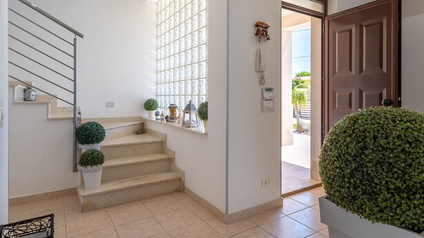 A staircase with a metal railing, a potted plant, a wall-mounted telephone, and a door leading to an outdoor area.