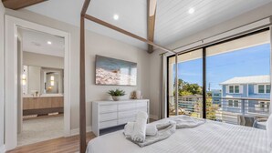 A modern bedroom with a large bed, a view of the city, and a bathroom with a vanity and mirror. - Welcome to Set in Sand! (Bradenton Beach)