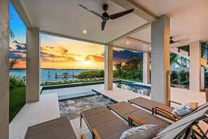 Une piscine à débordement située sur le toit, avec des chaises longues, un ventilateur de plafond et une vue imprenable sur le coucher de soleil sur l’océan.