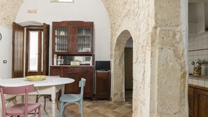 Een keuken met een witte betegelde vloer, een houten kast met glazen deuren, een televisie en een eettafel met stoelen.