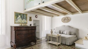 Een kamer met een houten plafond, een bed met een grijze deken, een houten dressoir, een klein tafeltje met een vaas en een vloer met een bloemmotief.