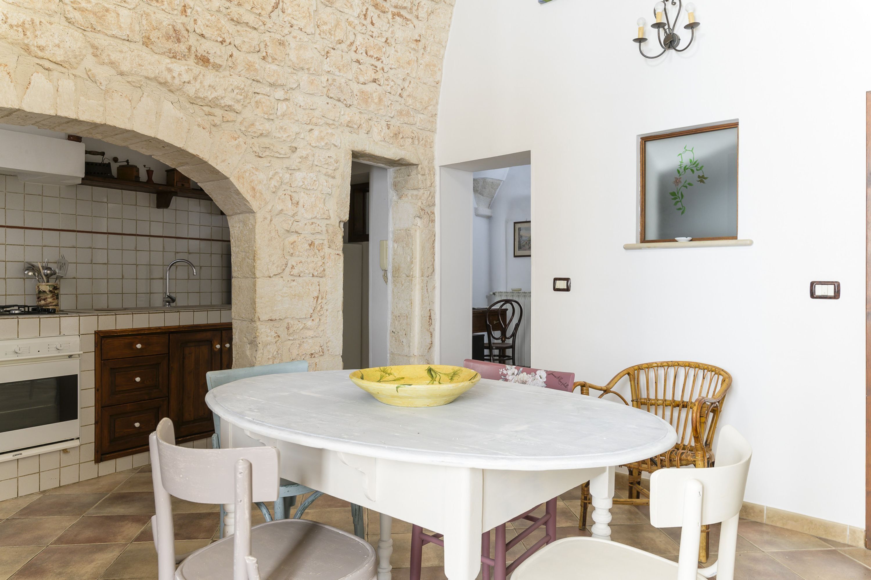 Una cocina con un arco de piedra, salpicadero de azulejos blancos, armarios de madera y una mesa de mármol blanco con sillas.