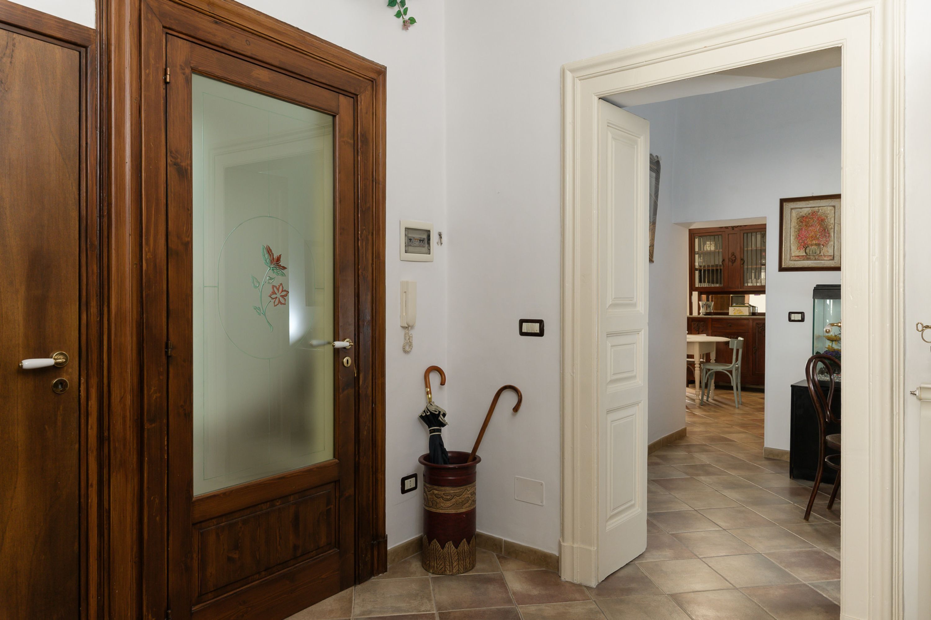 A hallway with a wooden door, a glass door, and a trash can with an umbrella.