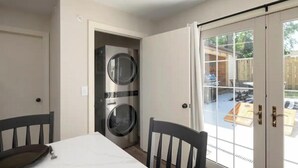 A room with a dining table, chairs, a washing machine, and a sliding glass door leading to an outdoor area. - Branson Downtown Trolley House (Branson)