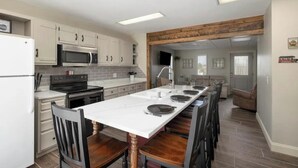 A modern kitchen with white cabinets, a large island, and a dining area with wooden chairs. - Branson Downtown Trolley House (Branson)
