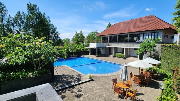 A swimming pool surrounded by lush greenery, a patio with outdoor furniture, and a modern house with a red roof. - PEPABRI Hotel & Resort (Cilimus)