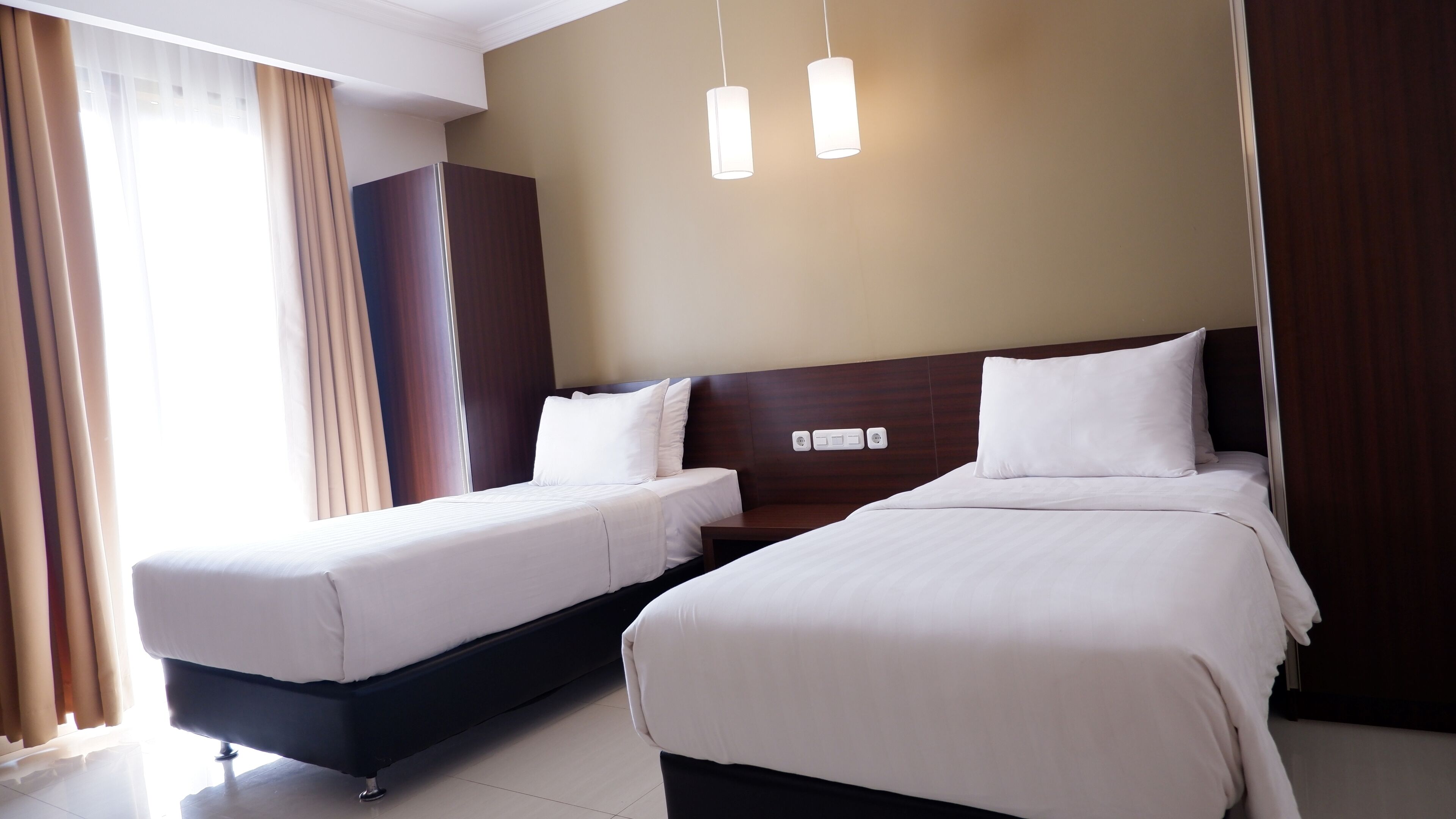 A hotel room with two beds, a wardrobe, and a nightstand.