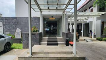 A modern building entrance with a covered walkway, steps leading to a glass door, and a parked car.