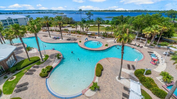 A large outdoor swimming pool with multiple sections, surrounded by palm trees and lounge areas. - FREE Daily Golf! Reflections 506 Amazing Views, Heated Resort Pool & Hot Tub! (Panama City)