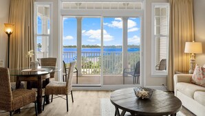 A room with a glass table, wicker chairs, a round wooden table, a sofa, and a view of the ocean through large sliding doors. - FREE Daily Golf! Reflections 506 Amazing Views, Heated Resort Pool & Hot Tub! (Panama City)